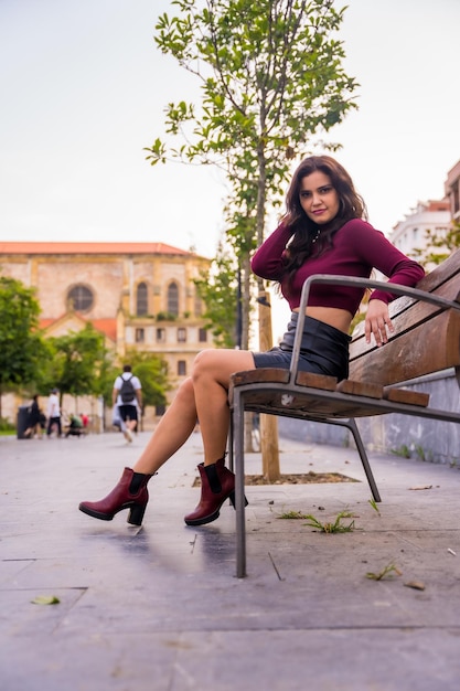 Una mujer morena en una falda de cuero sentada en la pose de moda de estilo de vida de la ciudad foto vertical