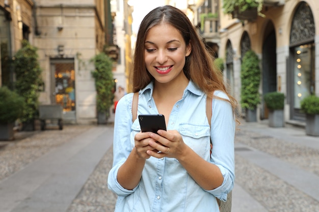 Mujer morena feliz escribiendo sms en smartphone en ciudad