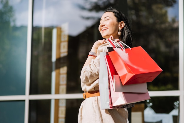 Mujer morena feliz sosteniendo bolsas de compras al aire libre. Mujer adicta a las compras satisfecha con las compras.