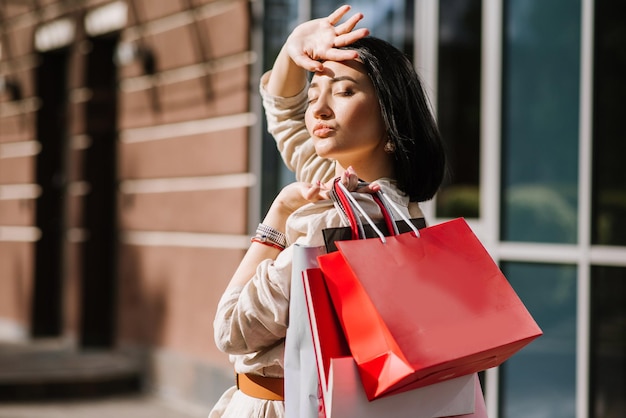 Mujer morena feliz sosteniendo bolsas de compras al aire libre. Mujer adicta a las compras satisfecha con las compras.