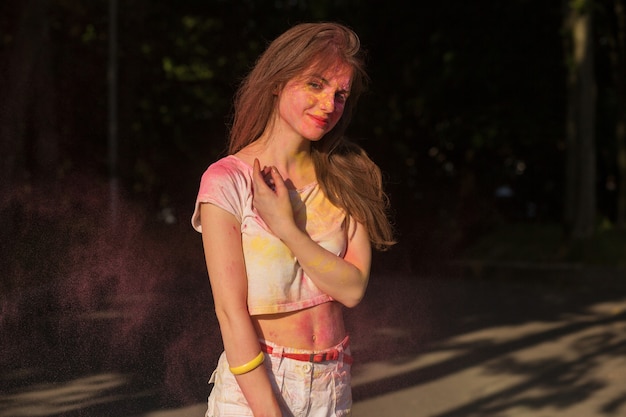 Mujer morena fresca posando cubierta con pintura Holi amarilla y rosa