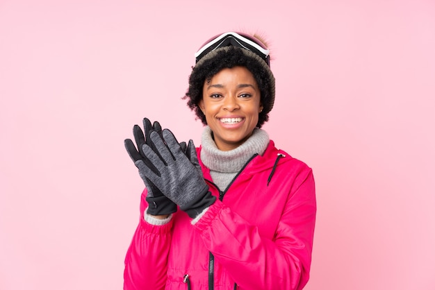 Mujer morena con gafas de nieve sobre fondo rosa aislado