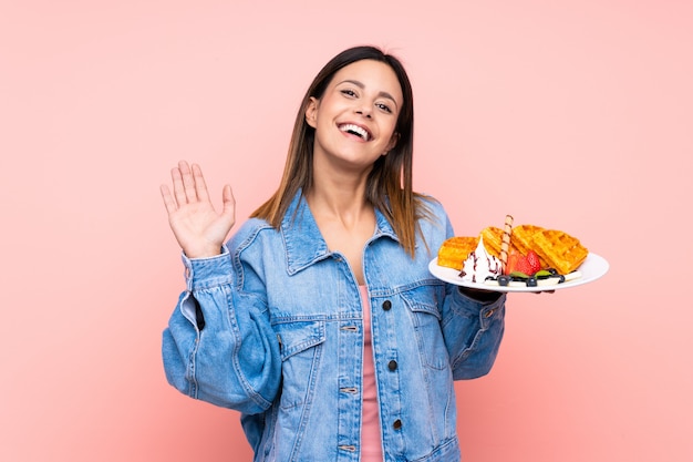 Mujer morena con gofres saludando con la mano con expresión feliz