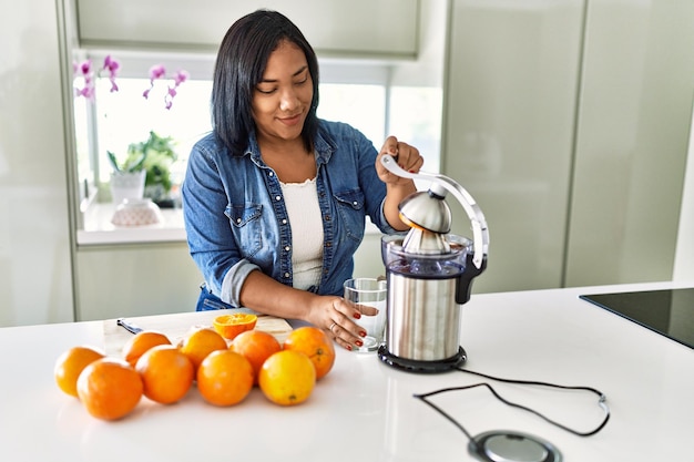 Mujer morena hispana preparando jugo de naranja en la cocina