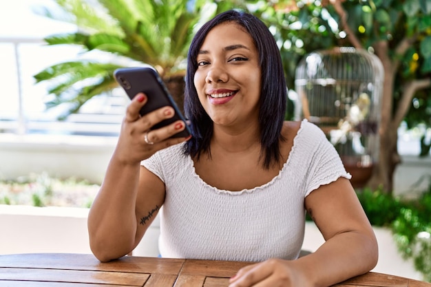 Foto mujer morena hispana sentada enviando mensajes de voz en la terraza