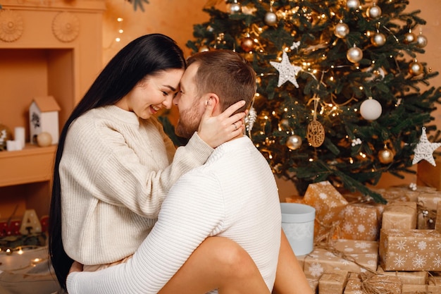 Mujer morena y hombre barbudo sentados cerca del árbol de Navidad y abrazándose