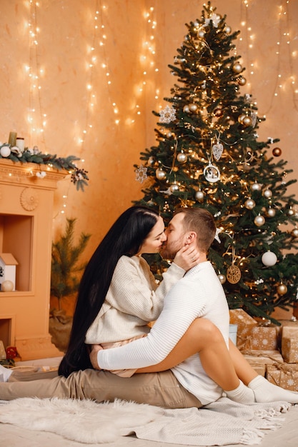 Mujer morena y hombre barbudo sentados cerca del árbol de Navidad y abrazándose