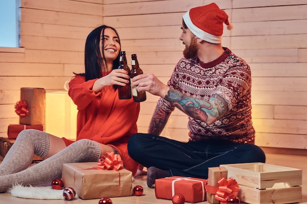 Mujer morena y hombre hipster barbudo beben cerveza y celebran la Navidad en casa.