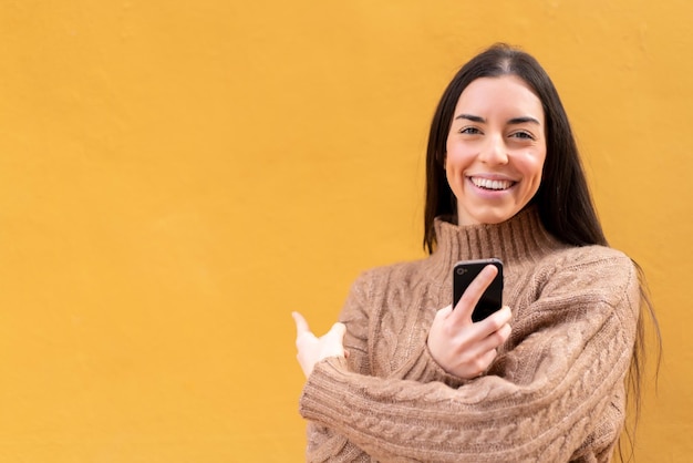 Mujer morena joven al aire libre usando teléfono móvil y apuntando hacia atrás