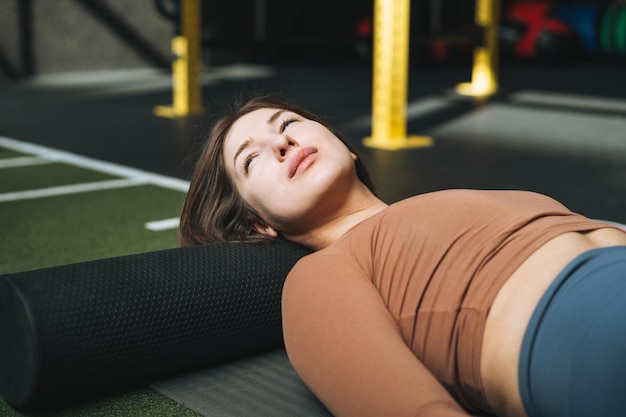 Mujer morena joven haciendo pilates de estiramiento en rollo de masaje en el gimnasio del club de fitness