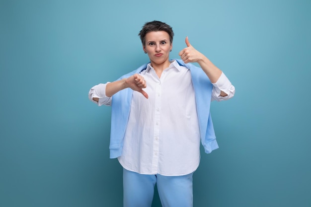 Mujer morena joven positiva enérgica con corte de pelo corto en camisa blanca que muestra gusto y disgusto