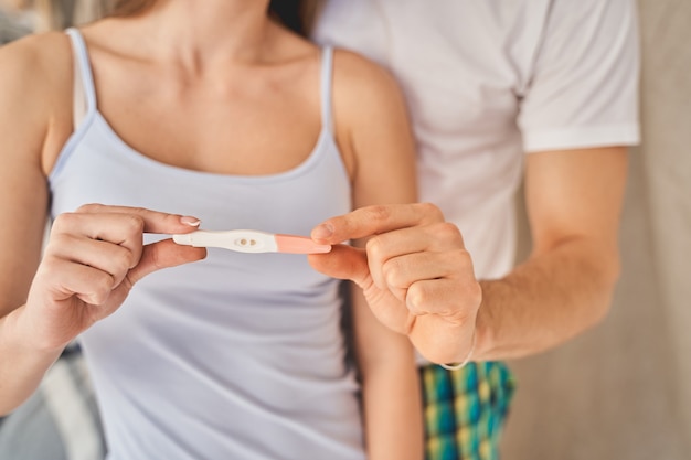 Mujer morena joven que demuestra los resultados de la prueba de embarazo mientras está de pie cerca de su novio. Concepto de salud y cuidado