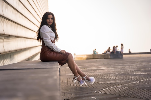 Mujer morena latina con falda de cuero sentada en la ciudad al atardecer