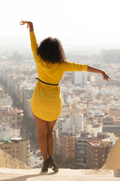 Mujer morena latina de risas con ropa amarilla baila en el fondo de la ciudad al aire libre