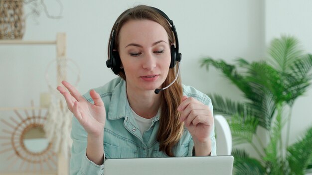 Mujer morena lleva auriculares llamando a charlas de portátil con el profesor en línea estudiando, trabajando desde casa.