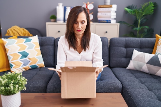 Mujer morena de mediana edad abriendo caja de cartón relajada con expresión seria en la cara simple y natural mirando a la cámara