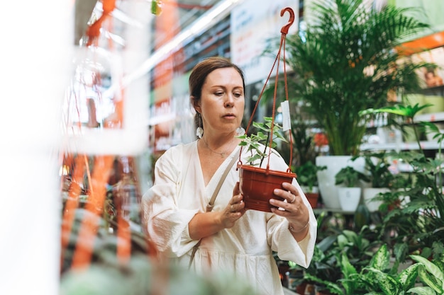 Mujer morena de mediana edad con vestido blanco compra plantas de interior en macetas verdes en la tienda de jardinería