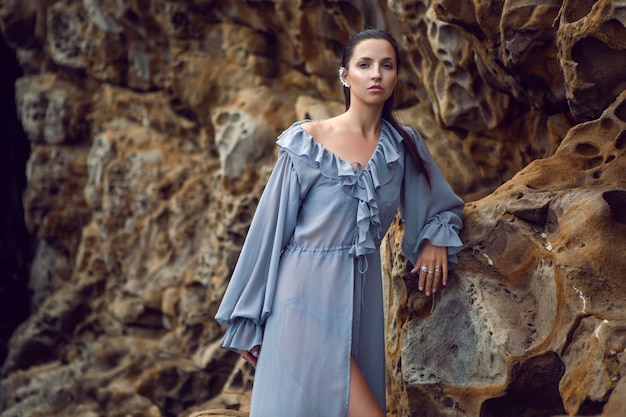 Mujer morena de moda con un vestido gris se encuentra en una roca de queso en el verano