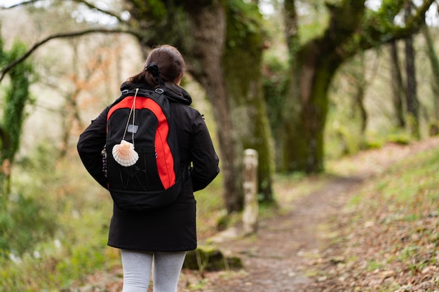 Mujer morena peregrina con cola de caballo y una concha colgante haciendo el Camino de Santiago