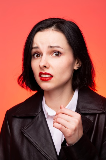 mujer morena con pintalabios rojo en los labios en una chaqueta de cuero negro y camisa blanca backgrou rojo