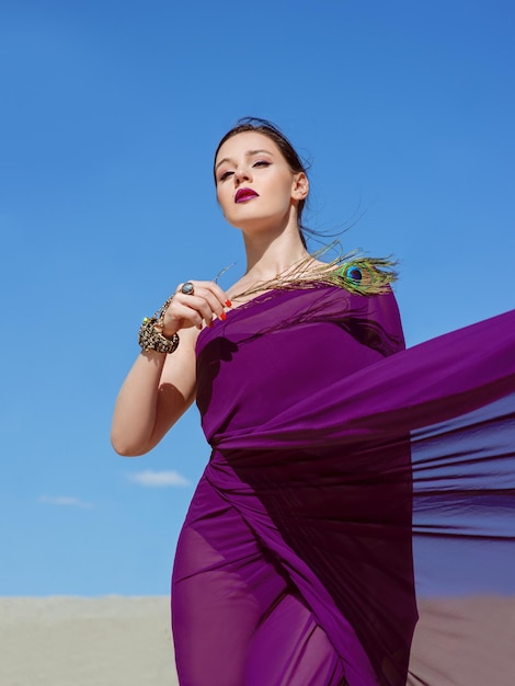 mujer morena con la pluma de pavo real en tela morada en el desierto