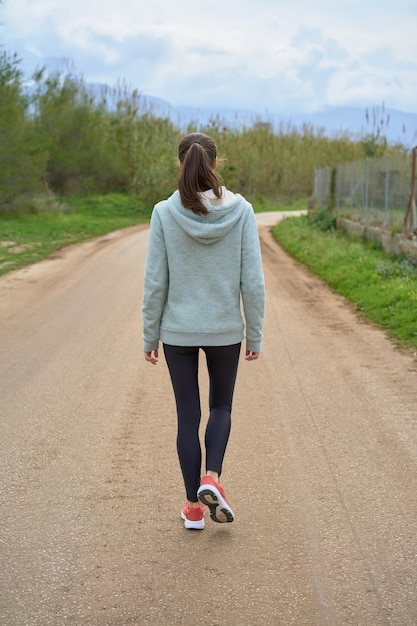 Mujer morena en polainas y sudadera caminando en el campo visto desde atrás