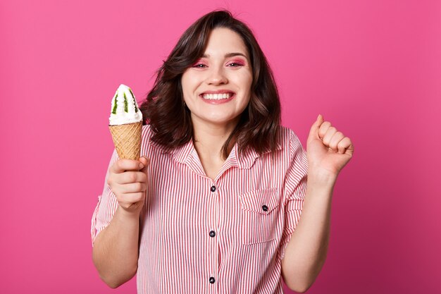 mujer morena positiva con porción de helado, sonriendo sinceramente, con expresión facial agradable