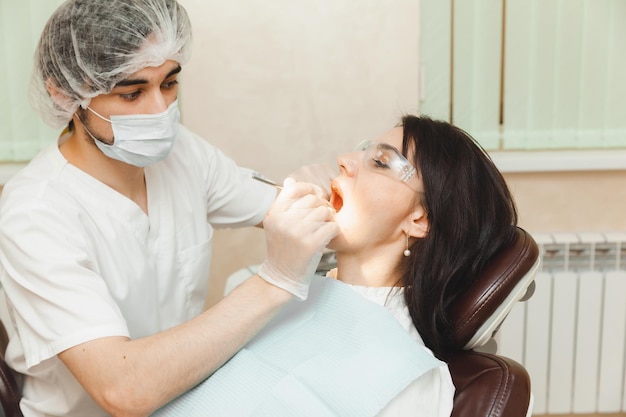 Una mujer morena positiva se sienta en el consultorio del dentista durante un chequeo dentista examinando los dientes de la mujer