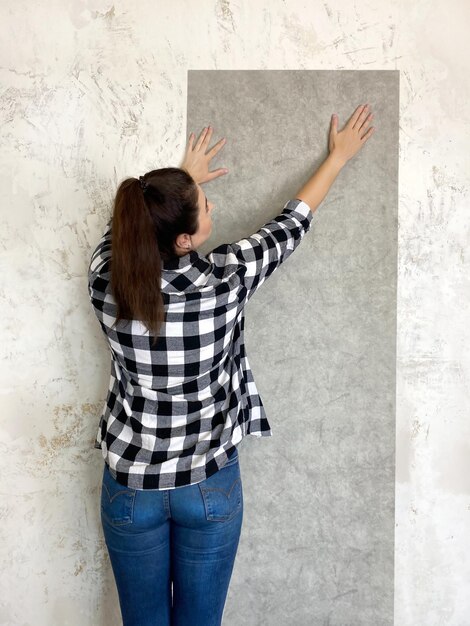 Foto mujer morena probando un nuevo papel tapiz en casa, una pared blanca recién pintada para un efecto visual