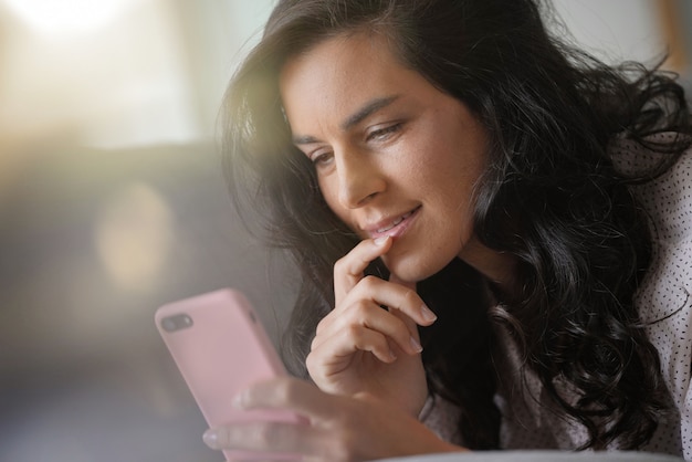 Mujer morena que se relaja en el sofá, conectado con el teléfono inteligente