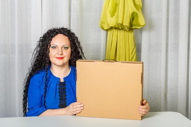 Foto una mujer morena rizada y alegre se sienta en una mesa en la oficina sosteniendo una copia de una compra de lugar