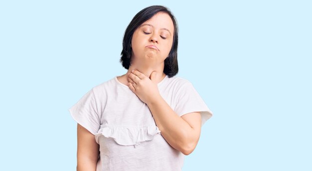 Mujer morena con síndrome de down con camiseta blanca casual tocando el cuello doloroso, dolor de garganta por gripe, terrón e infección