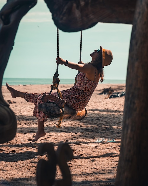 Mujer morena con sombrero disfrutando de la playa en un columpio