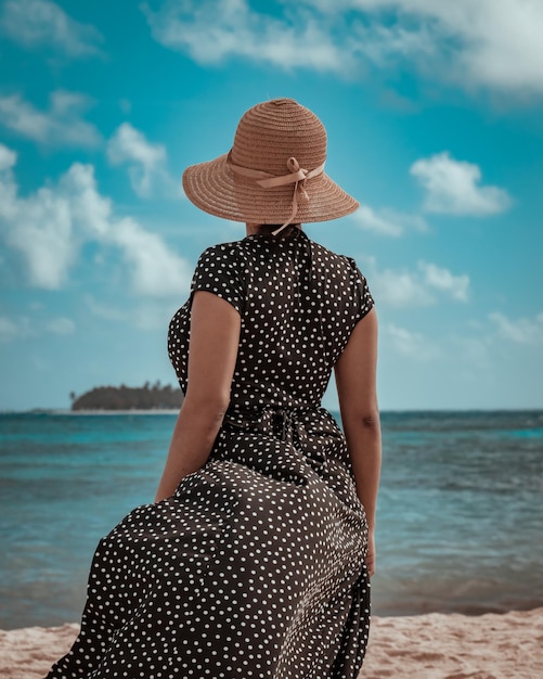 Mujer morena con sombrero mirando una isla desde la playa