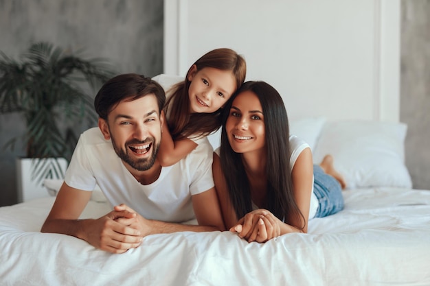 Mujer morena sonriente descansando en una cama mientras su marido y su hija se ríen alegremente a su lado