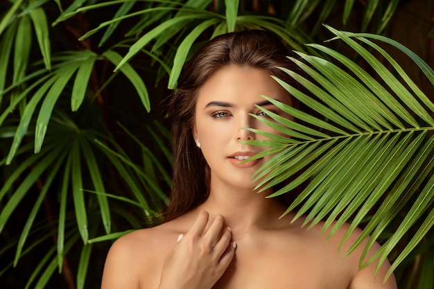 Mujer morena sonriente joven con la hoja verde grande, cierre del concepto de la gente del cuidado del balneario para arriba