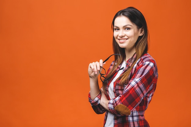 Mujer morena sonriente en lentes y presentación casual con los brazos cruzados y mirando a la cámara sobre fondo naranja.