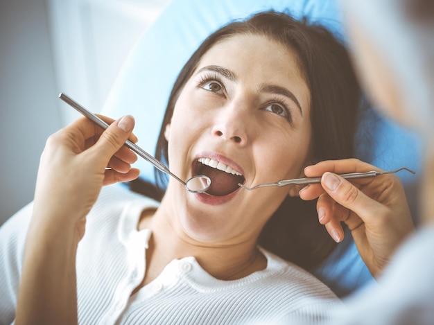 Mujer morena sonriente siendo examinada por un dentista en la clínica dental. Manos de un médico que sostiene instrumentos dentales cerca de la boca del paciente. Dientes sanos y concepto de medicina.