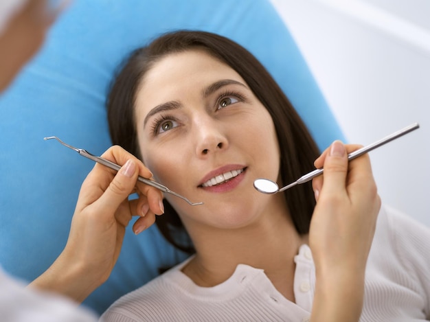 Mujer morena sonriente siendo examinada por un dentista en la clínica dental. Manos de un médico que sostiene instrumentos dentales cerca de la boca del paciente. Dientes sanos y concepto de medicina.