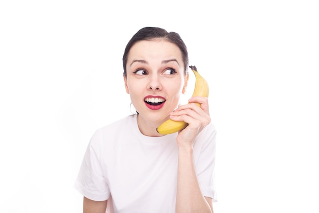 Mujer morena sonriente sosteniendo plátano como fondo de estudio blanco de teléfono