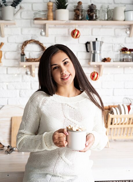 Mujer morena sosteniendo una taza de cacao de malvavisco en la cocina