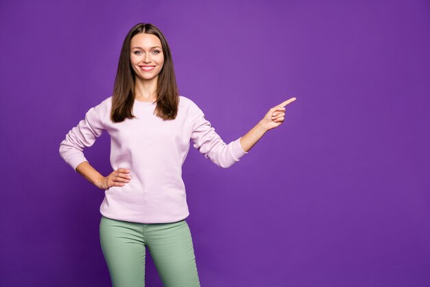 Mujer morena en suéter pastel posando contra la pared púrpura