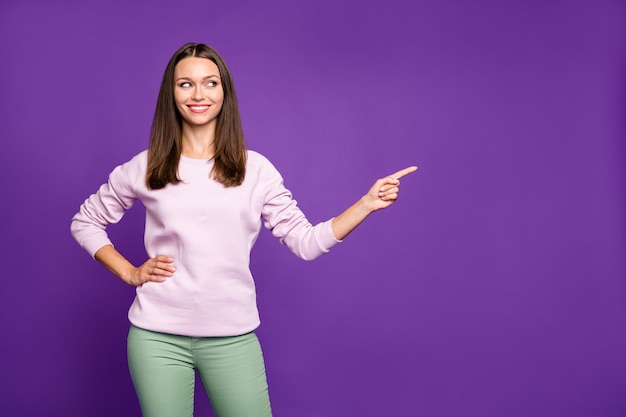 Mujer morena en suéter pastel posando contra la pared púrpura