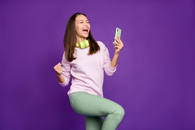 Mujer morena en suéter pastel posando contra la pared púrpura