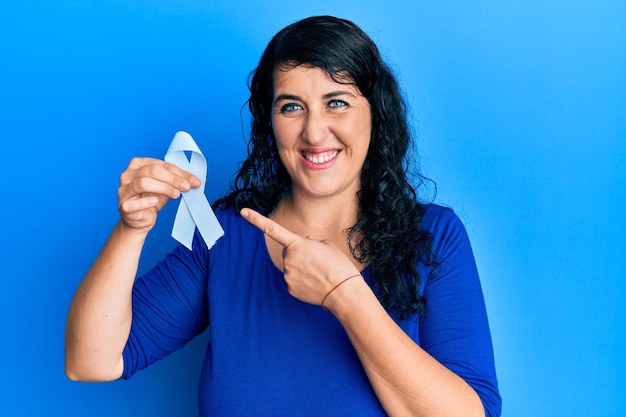 Mujer morena de talla grande con cinta azul sonriendo feliz señalando con la mano y el dedo