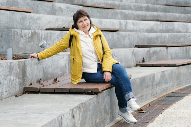 La mujer morena de la tercera edad se sienta en un parque de la ciudad en los escalones y mira hacia otro lado