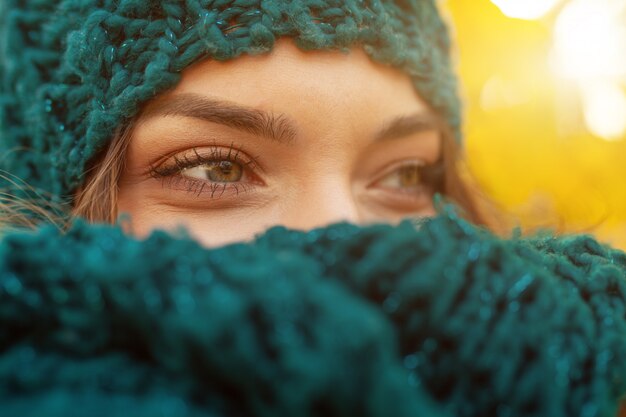 Mujer morena tímida joven natural hermosa con los ojos sonrientes que llevan la bufanda hecha punto