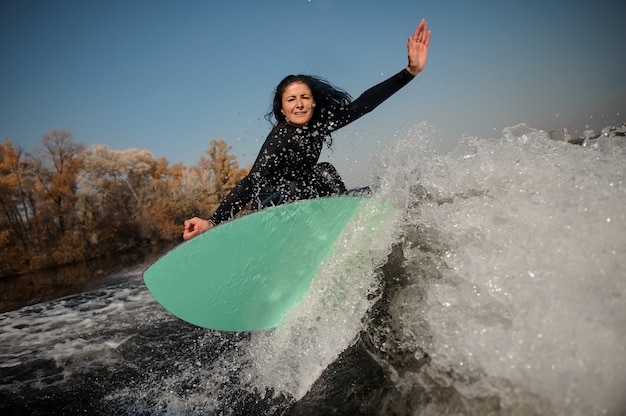 Mujer morena en traje de baño blanco saltando sobre el wakeboard verde sobre las rodillas dobladas