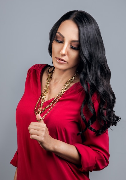 Mujer morena vestida con camisa roja y sosteniendo una cadena de oro