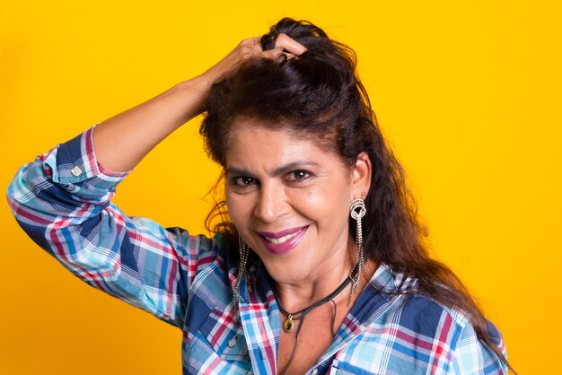 Foto mujer morena vestida de personaje con pantalones y camisa a cuadros con la mano en la cabeza celebración de junio de la fiesta de sao joao aislada sobre fondo amarillo